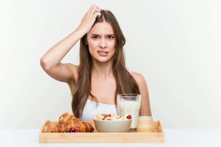 Sieviete apjukusi pie brokastu galda — piena glāze, pārslas un maize; izteikts apjukums par uzturu, ja trūkst olbaltumvielas.