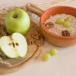 Šķiedrvielām bagāti produkti: ābols, auzu pārslas, rieksti un vīnogas uz galda