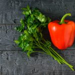 Karotinoīdi – sarkana paprika un pētersīļi uz tumša koka galda