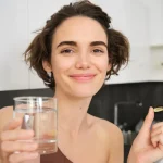 Sieviete ar glāzi ūdens un uztura bagātinātāju kapsulu – arginīna lietošana veselībai.