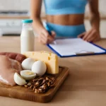 Produkti kas satur daudz olbaltumvielas uz virtuves galda ar olām, gaļu un piena produktiem